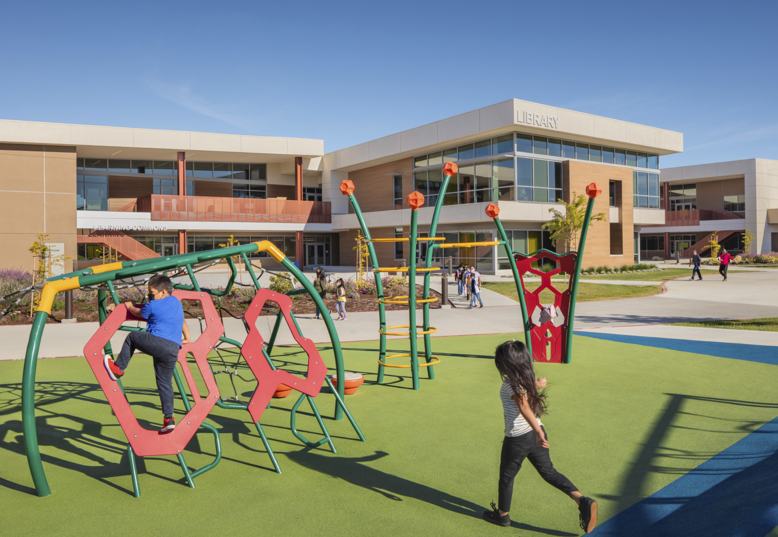 Bill Libbon School front entrance, with kids playing on a colorful playground on green padding. 2 story school behind