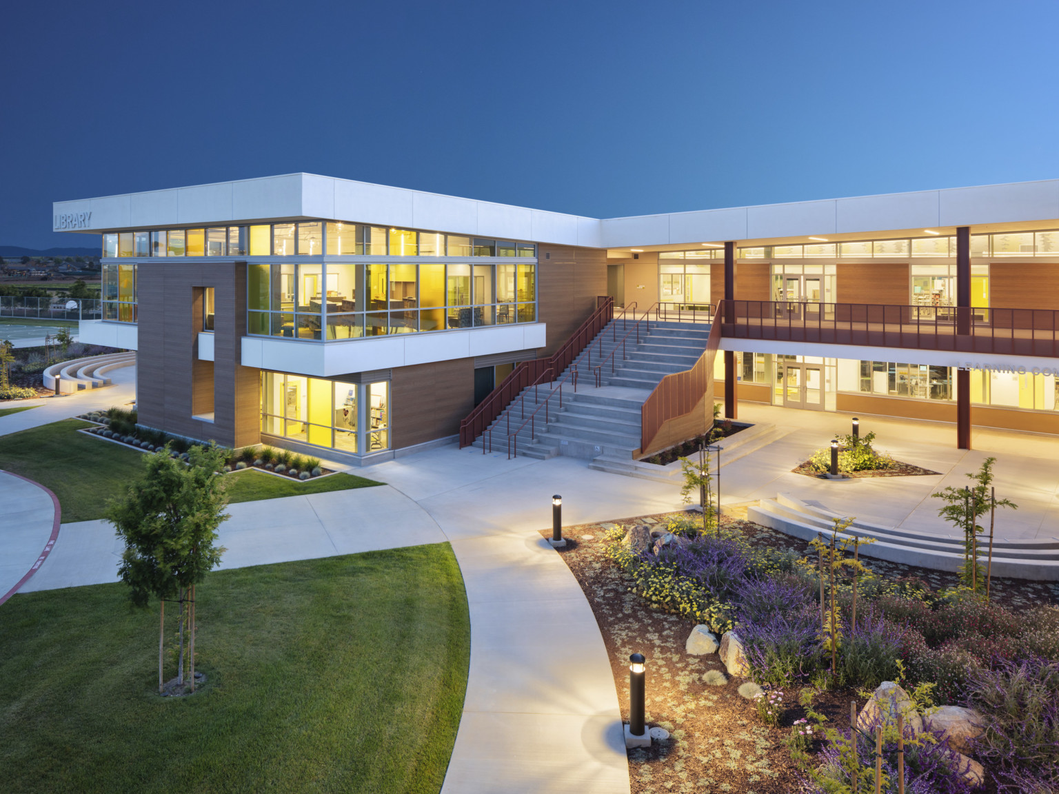 School library and entrance illuminated at night through floor to ceiling windows. Steps to 2nd floor right of library