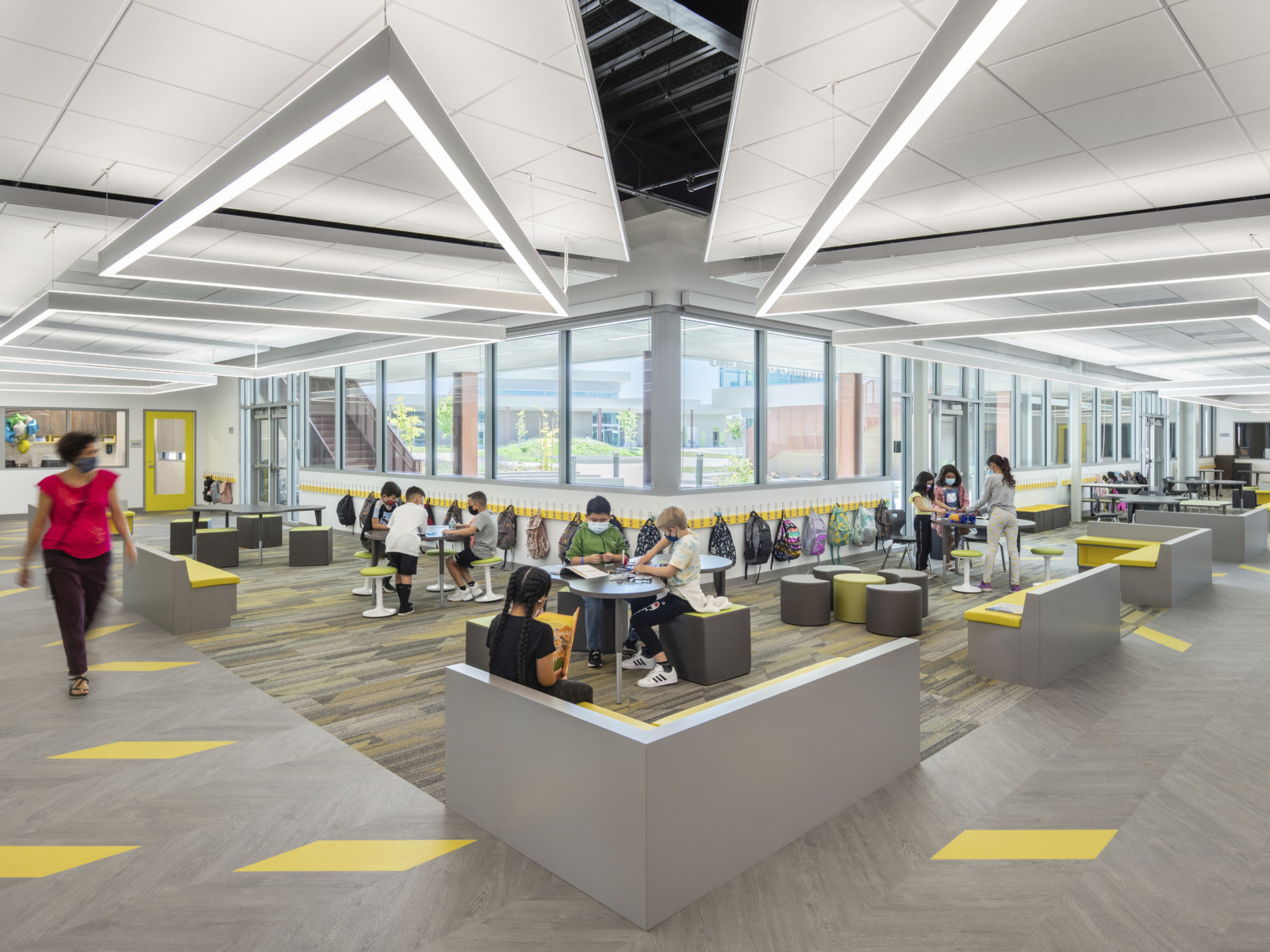 Corner of hallway with beige and yellow floor tiles. Seating area lines both walls, connecting at corner. White drop ceiling