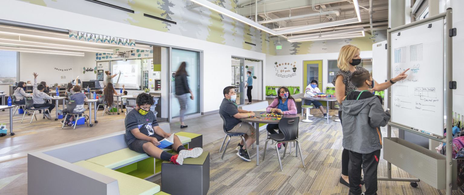 Learning space with benches separating from hallway with green pattern lining upper wall. Flexible wall on classroom, across