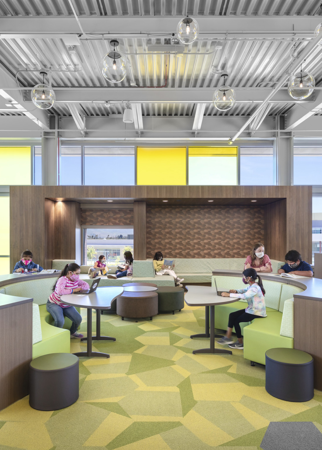 Seating area with rounded green couches and stools. Behind, dark wooden alcove with learning space inside and recessed space