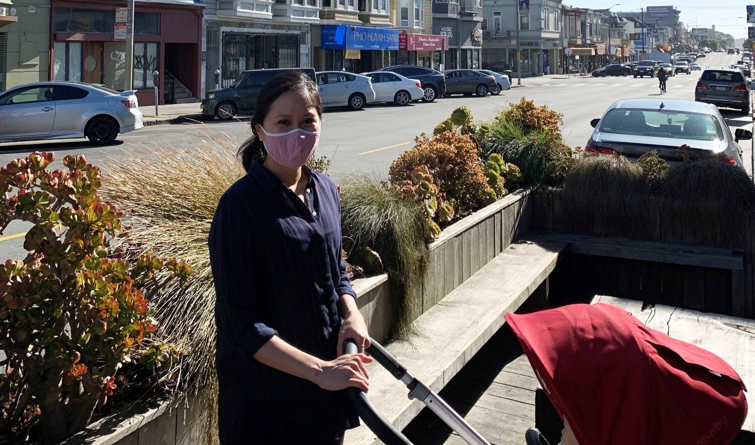 Catherine Meng pushing a red hooded stroller in an outdoor seating area on a street with row buidlings