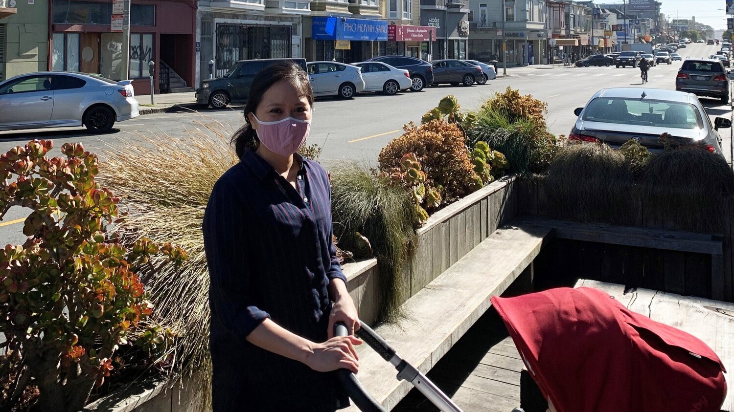 Catherine Meng pushing a red hooded stroller in an outdoor seating area on a street with row buidlings