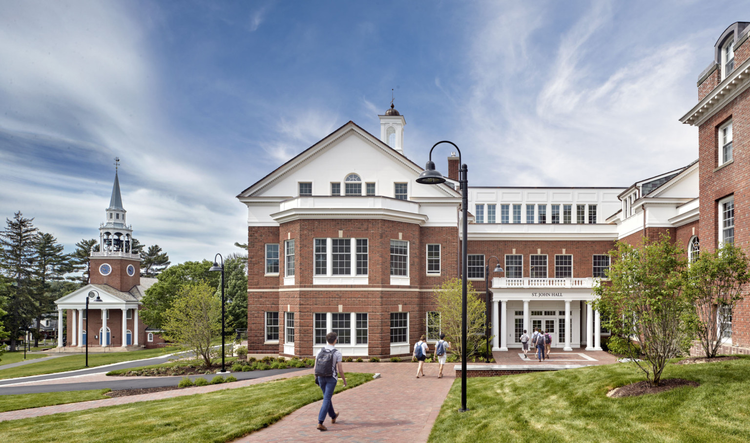 a brick building with white detailing and a brick pathway lead to a pillared entrance