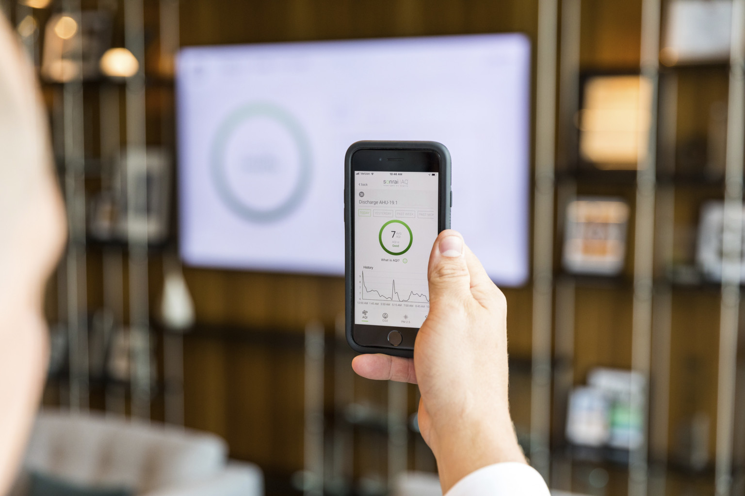 person using sonrai IAQ app in a space to read live air quality metrics, which are also shown on the lobby screen in front person using sonrai IAQ app in a space to read live air quality metrics, which are also shown on the lobby screen in front