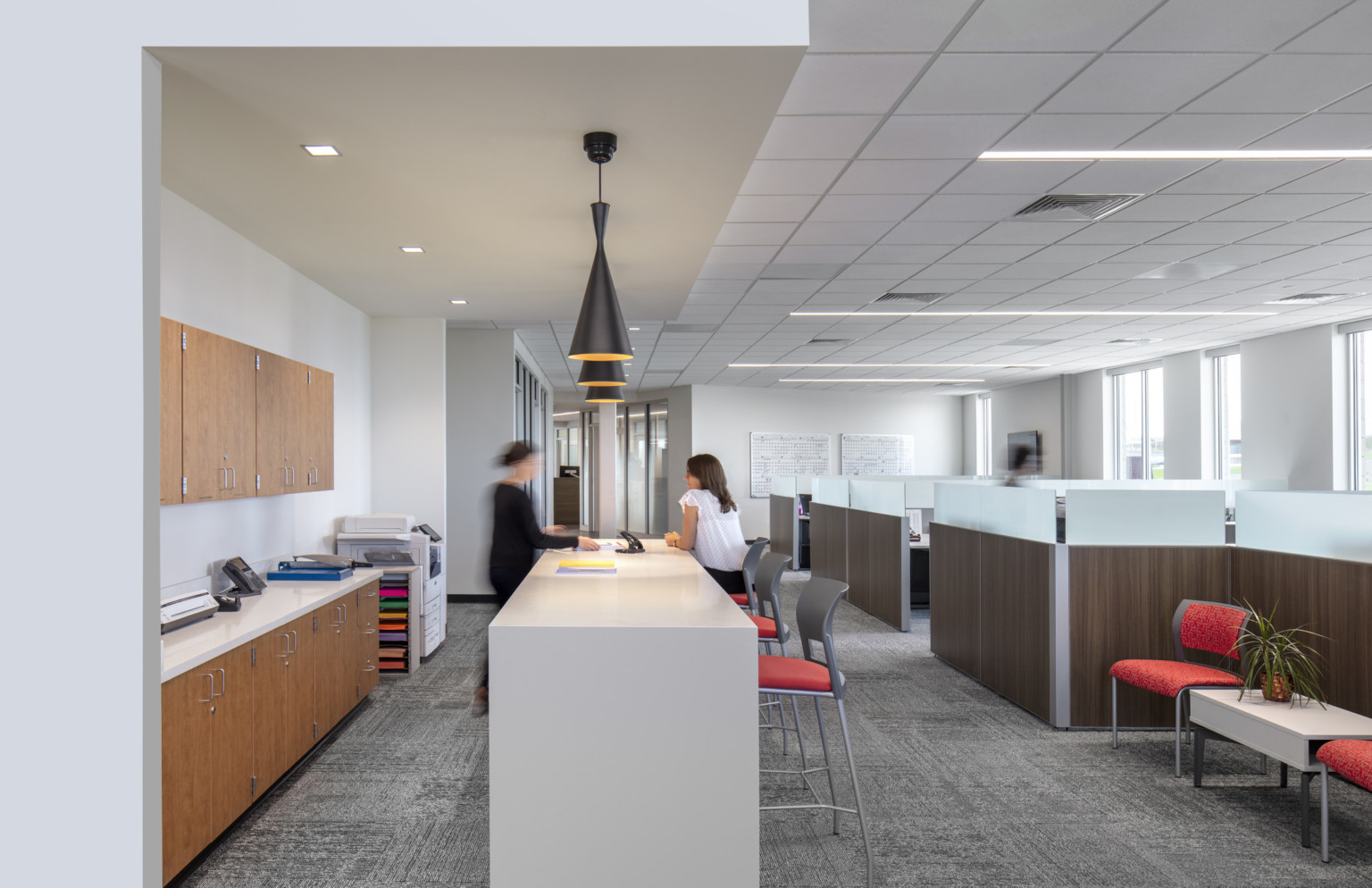 white standing height table under pendant lighting next to work stations and a seating area under drop ceiling detail