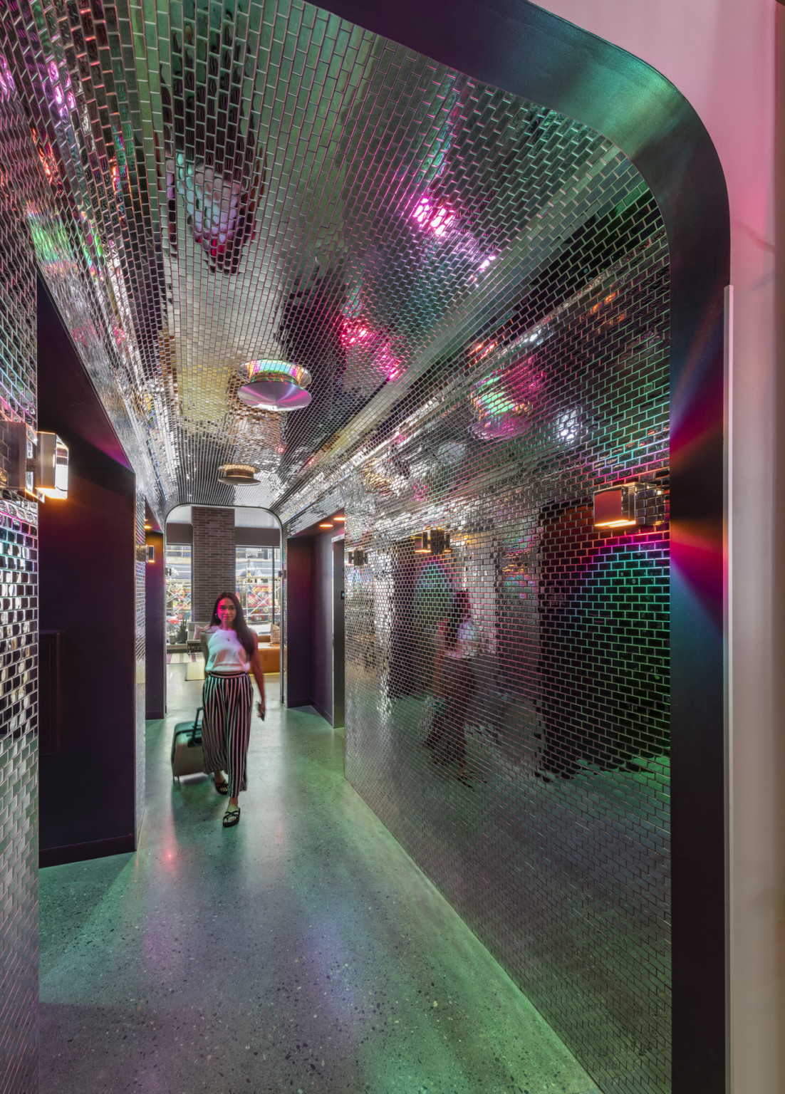 View through black doorway of hallway with reflective dark rectangular tiles on wall and ceiling, metallic lights on both