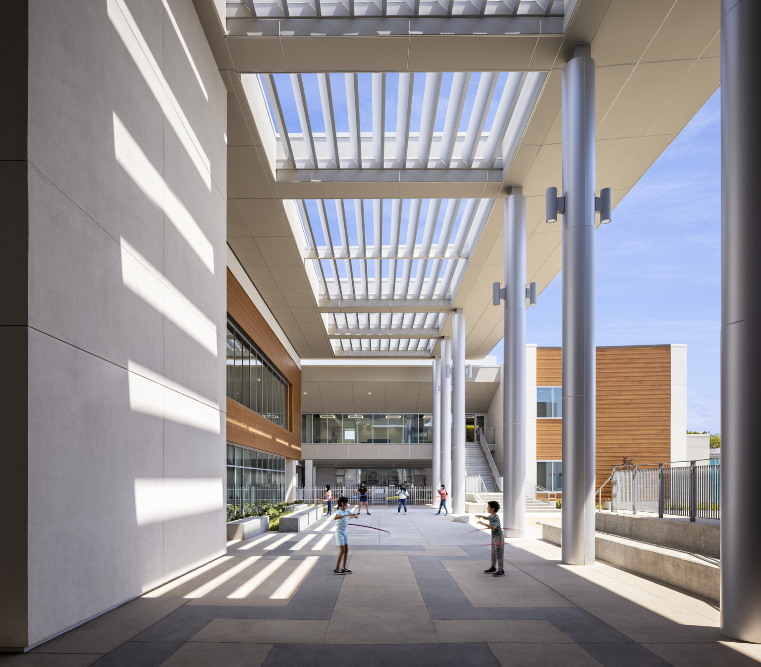 Front entrance partially cover under white canopy. Ahead, a 2nd floor walkway right of a large staircase to upper level