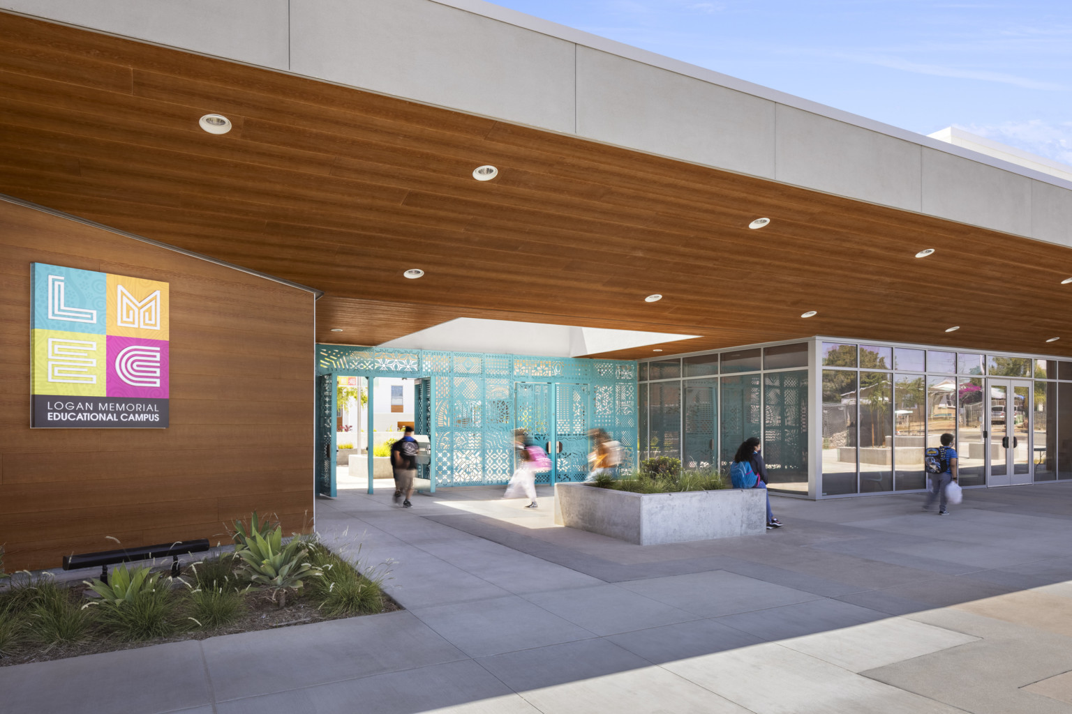 A blue metal patterned gate is recessed under a white overhang with wood panels underneath and a skylight at center