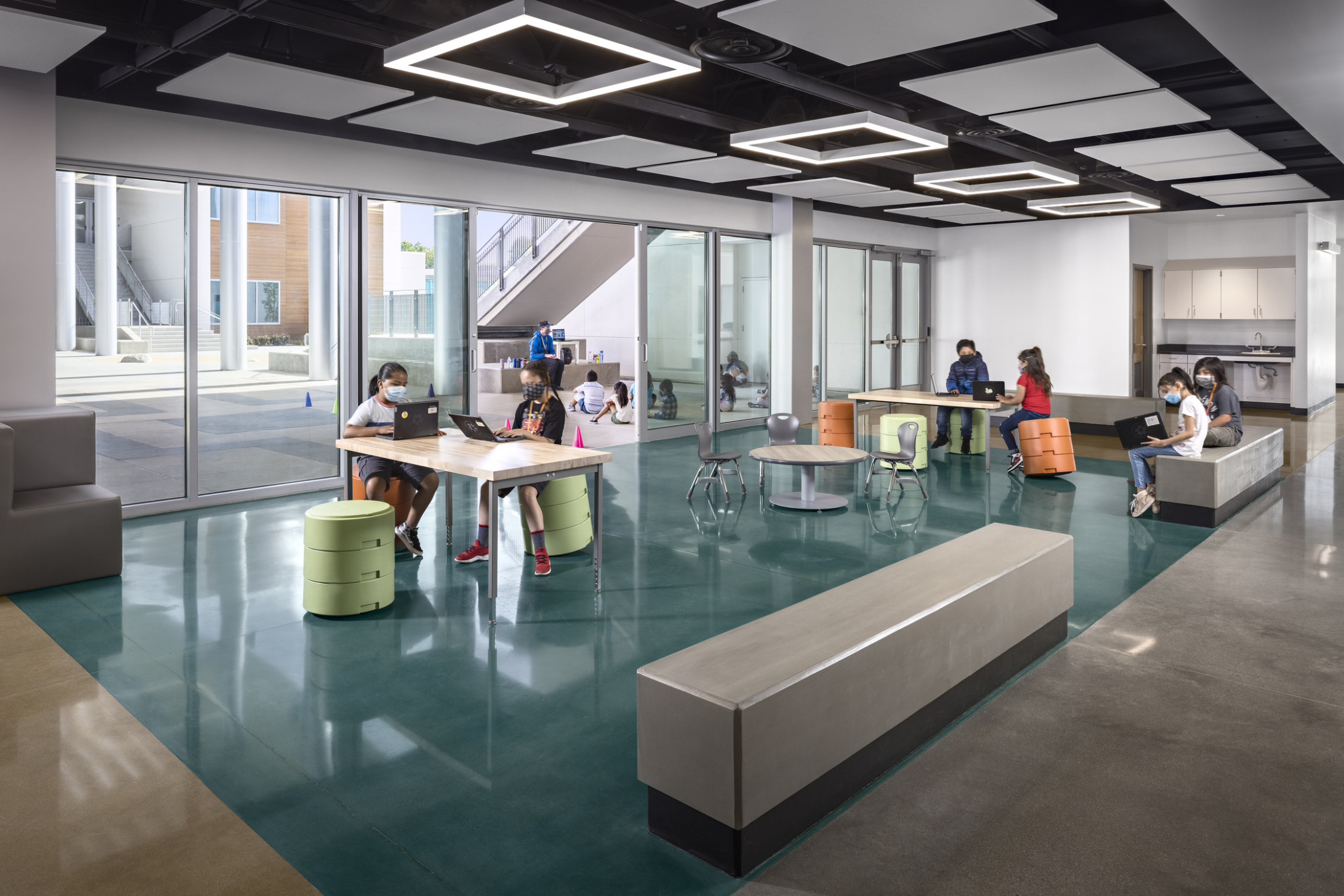 Logan Memorial Educational Campus seating area in white room with glass wall to outside; black ceiling with grey square drop ceiling details and lights; modern school design