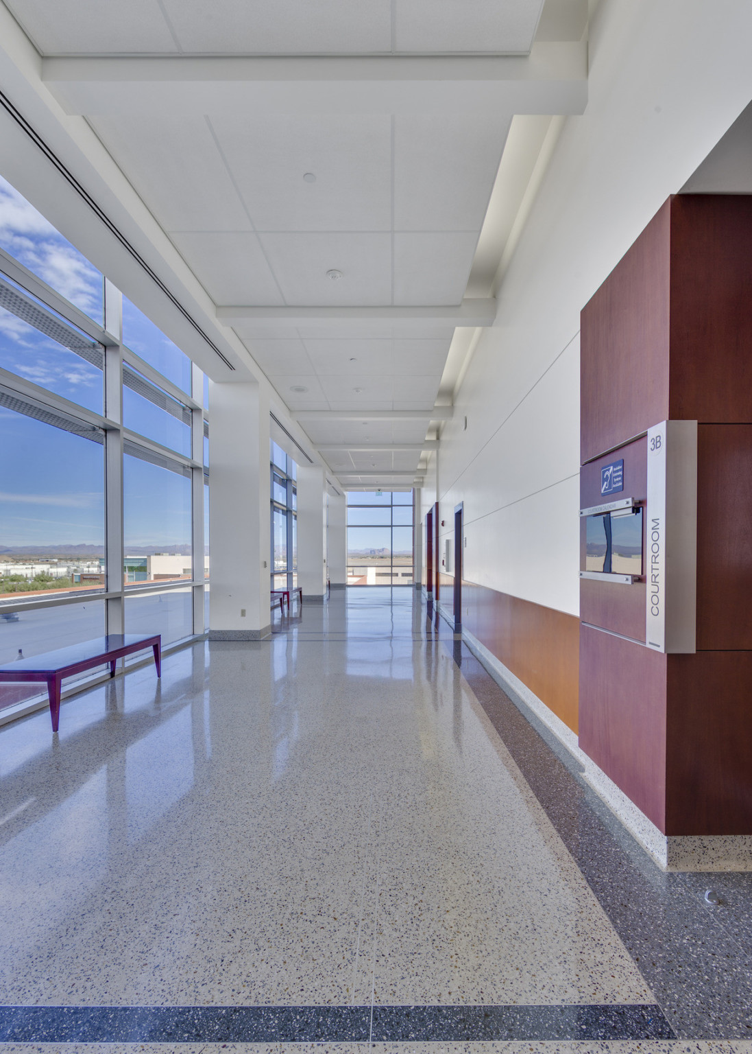 corridor inside Pinal County Courts building with floor to ceiling windows left and center, white wall with wood base, right corridor inside Pinal County Courts building with floor to ceiling windows left and center, white wall with wood base, right