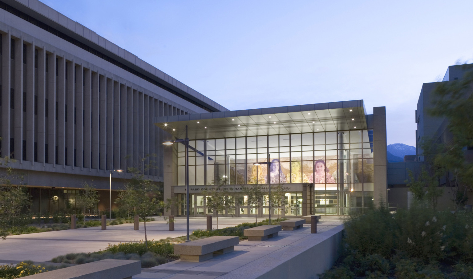 exterior view of El Paso County Courthouse lobby with triple height glass entrance and large mural inside. Treelined path