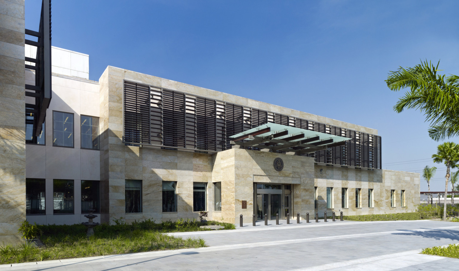 daytime view of 2 story stone building entrance with awning over doors and sunscreens on upper level windows