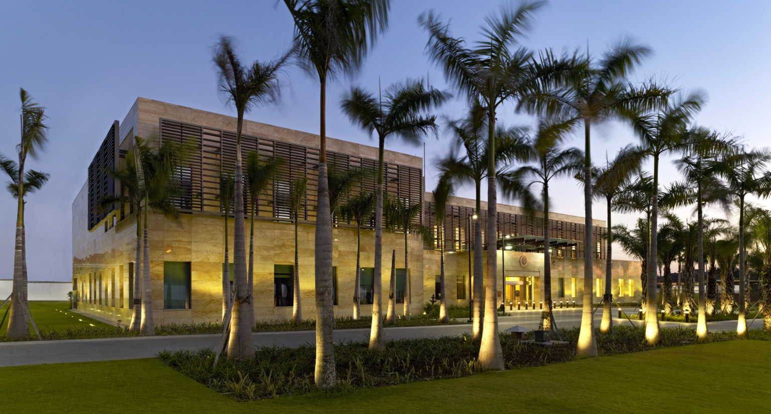 evening exterior view of US Consulate in Surabaya, Indonesia with palm trees and lighting features
