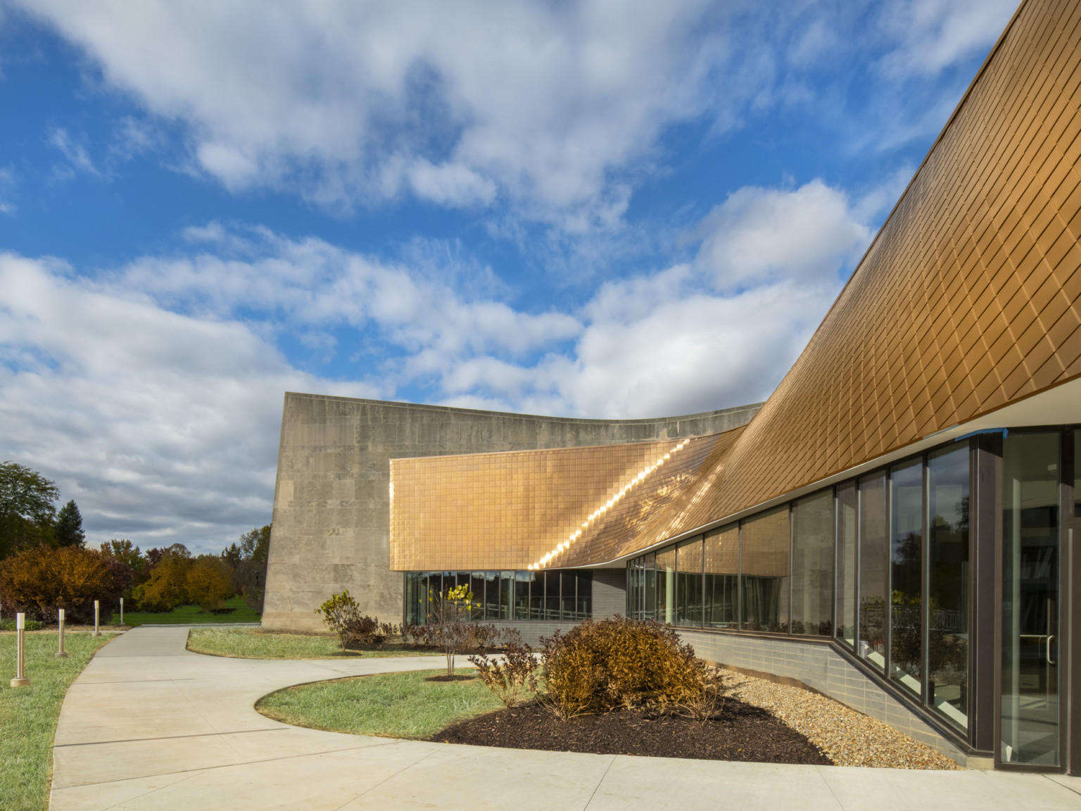 Copper tiled overhang of windowed entryway sits in front of stone building wall, mirroring some of the buildings curves