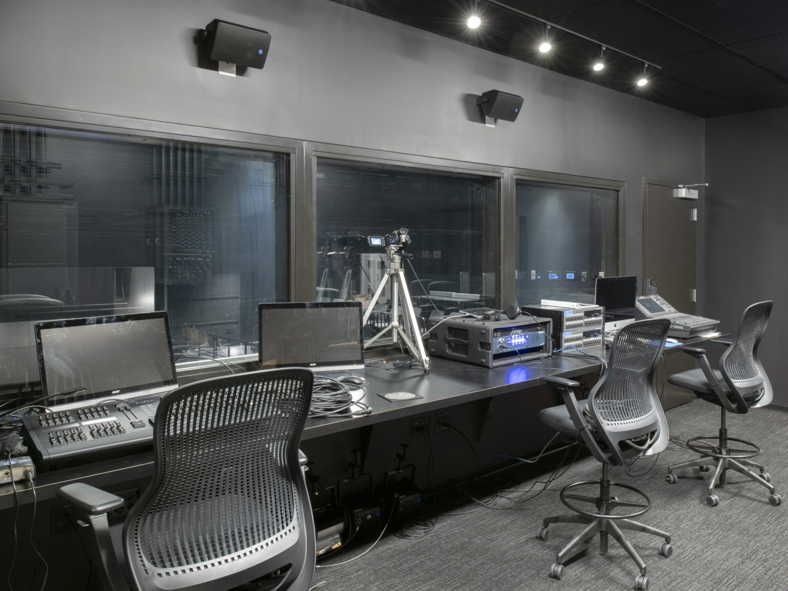 Grey room with three windows in front of a long table with computers and control systems