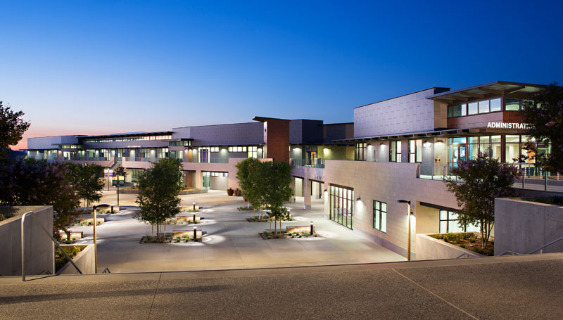 orthogonal tile and concrete building with glass windows and landscaped courtyard set into a recessed cliffside at dusk