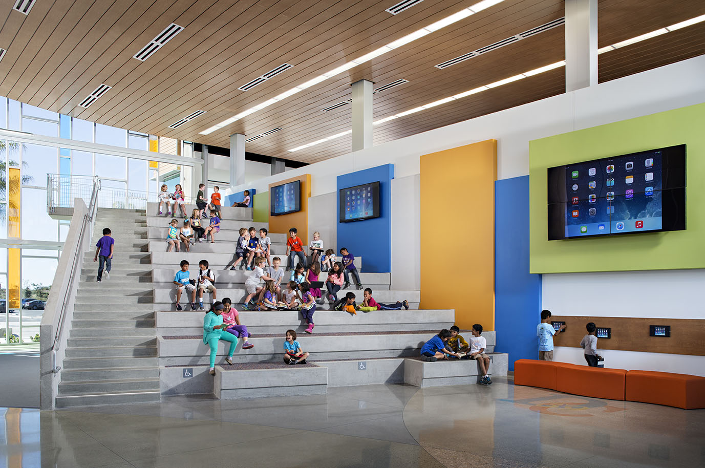 wood ceiling over concrete bleacher seating against a wall with blue orange and green panels and ipads and screens embedded