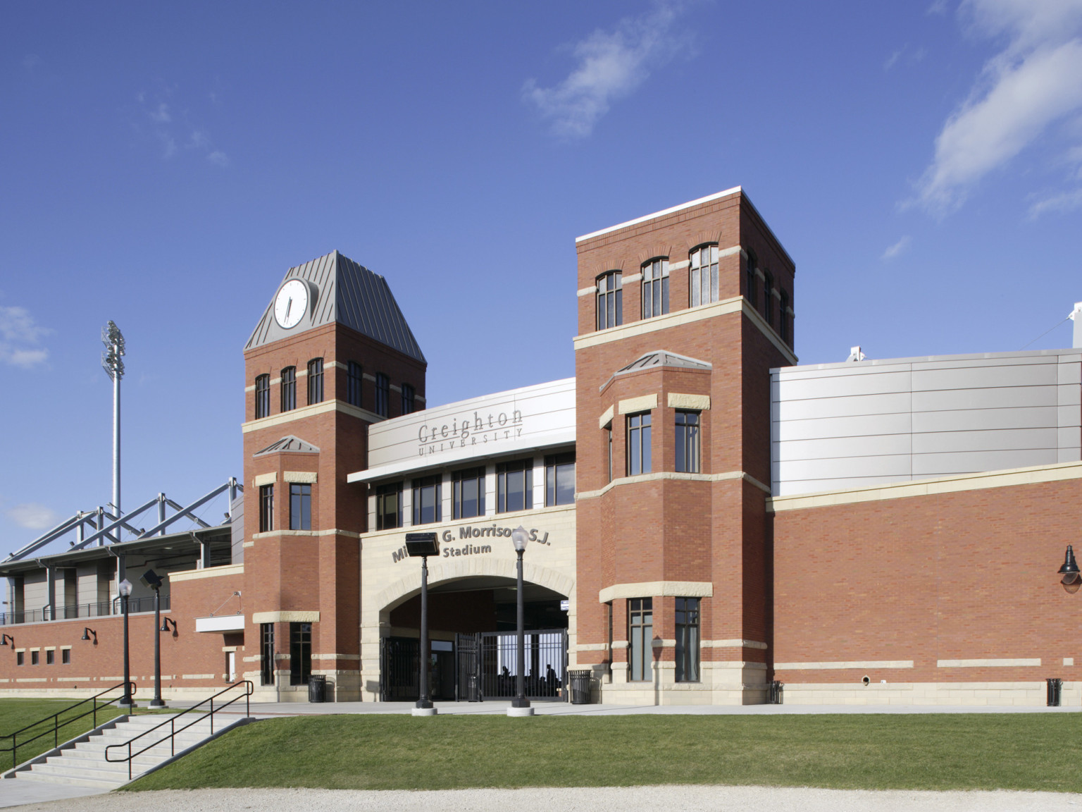 Arched stadium entry framed by brick towers and building. Right wall has brick base and silver panel upper level