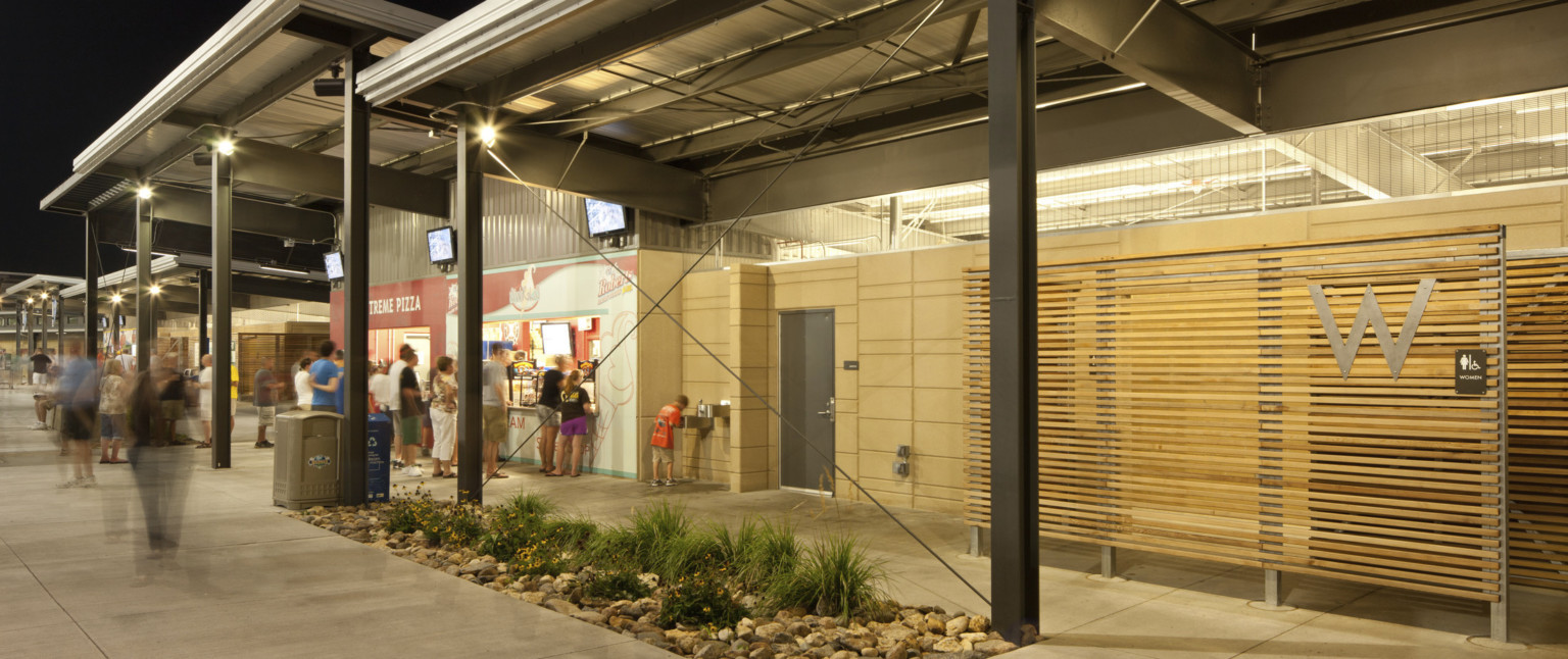 Silver awnings supported by exposed black beams over concession stands. Right, wood panel restroom entrance