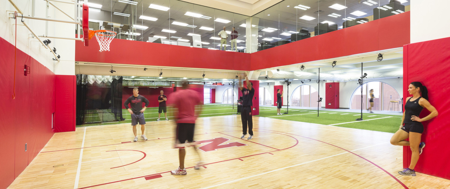 Double height basketball half court with floor to ceiling windows on 2nd floor. Turf floor on sides, arched windows to right