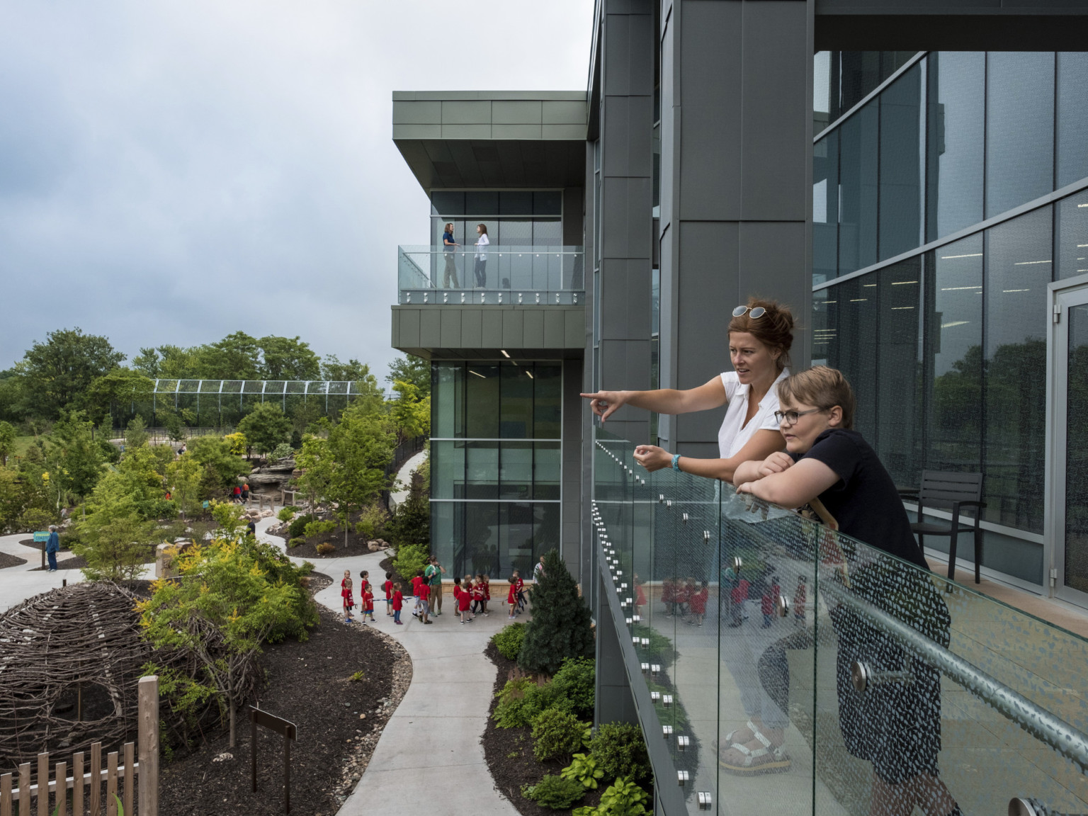 Glass walled balconies on 2nd and 3rd floors of grey window lined building look out onto Omaha Zoo