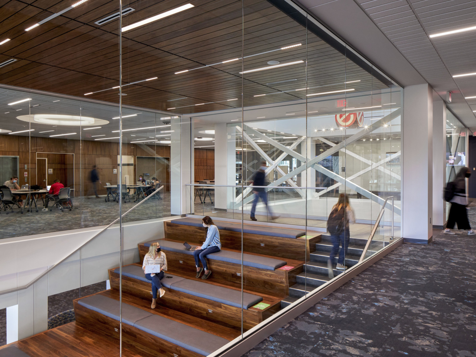 Top of glass walled staircase. Grey stairs have cushioned wood bench step seating.