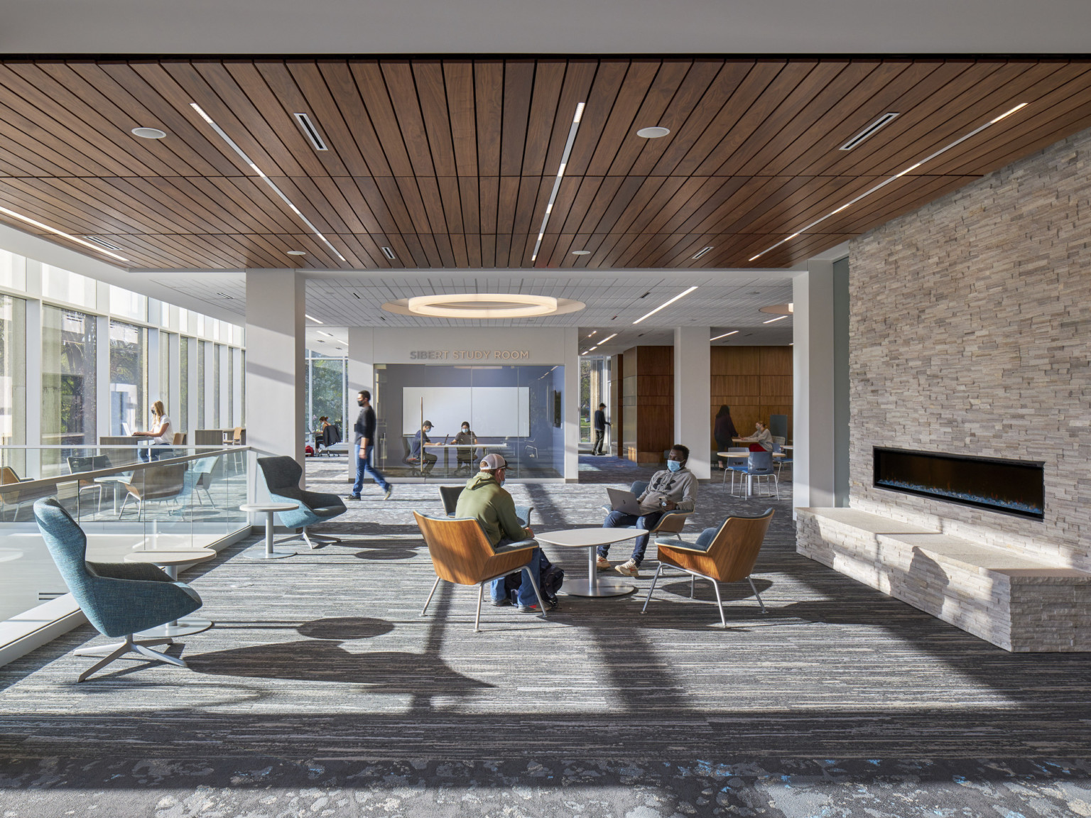 Seating area with tables and chairs next to fire place in room with wood panel ceiling with recessed lines of light