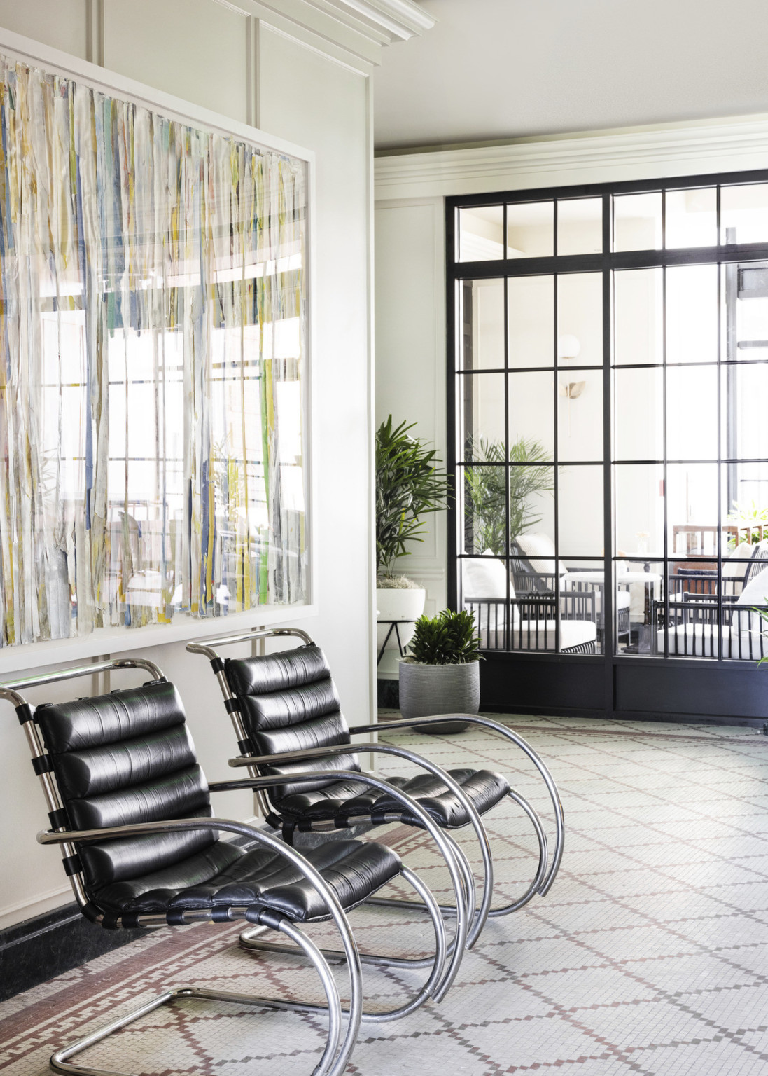 Grey and red tiles in white hallway with large window into next room. 2 black cesca arm chairs sit under framed abstract art