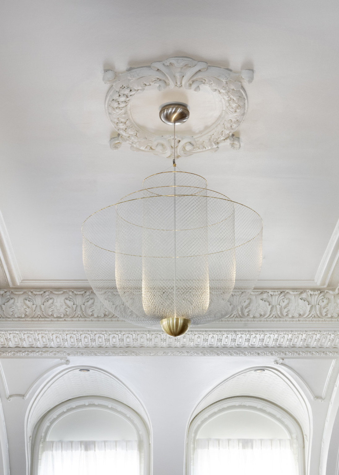 Close up view of hanging light fixture with 3 fishnet bowls which layer shorter and wider from the center, with gold rims