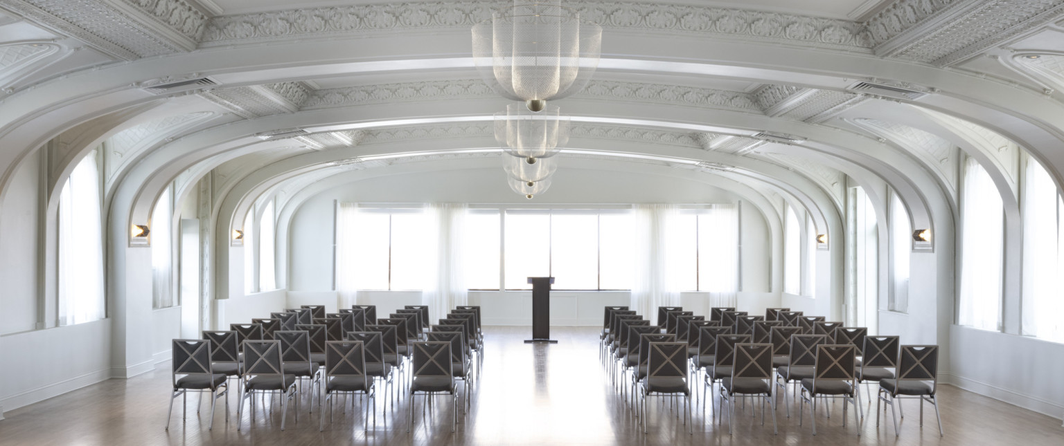 White arched room with recessed ceiling details with molded borders. Chandelier lighting down the center of the room