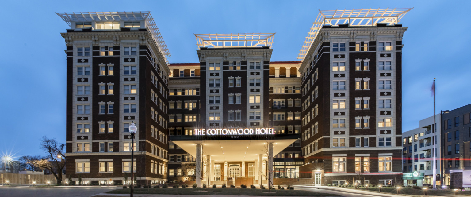 Front entry to The Cottonwood Hotel, an 8 story brick building with white stone details. Lit shelter from doors over driveway