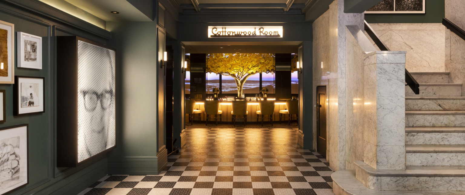 Black and white tiled entry to double doors of the Cottonwood Room, bar illuminated in the next room with yellow tree center