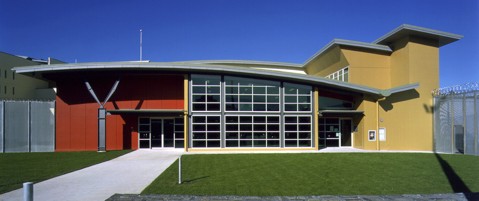 Closeup of entry. Double doors are to the left in a red painted portion, the rest of the building is painted a yellow brown