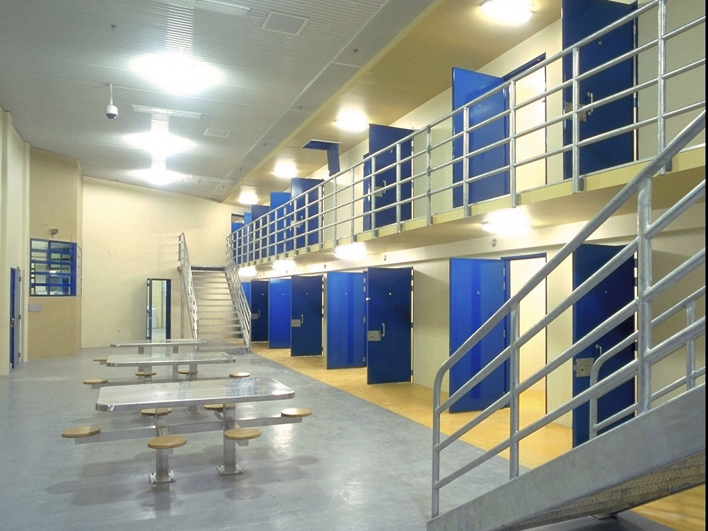 2 levels of cells with blue doors leading to central area with tables and seating at lower level