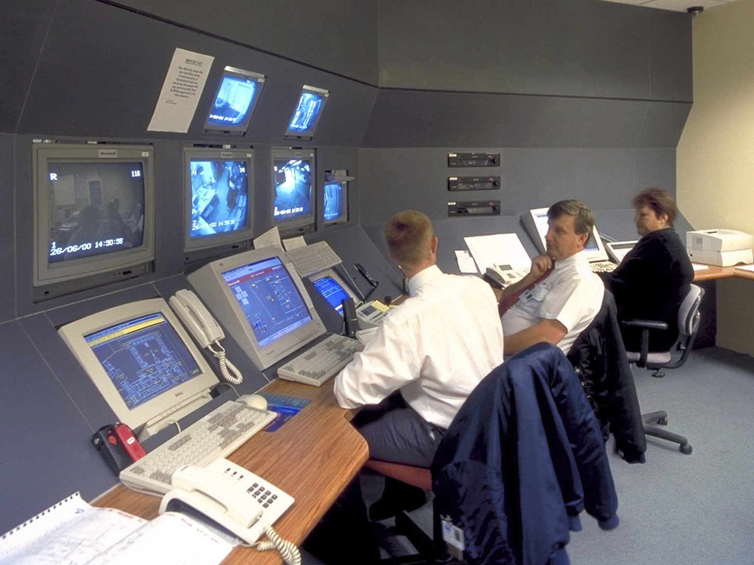 Guard station with wood desk and screens to monitor inmates in a grey room