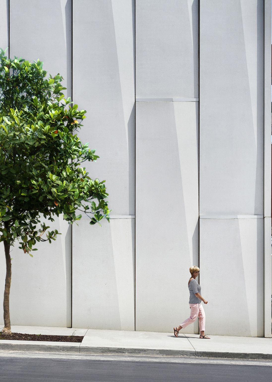 Textured white panels on exterior wall along treelined side walk