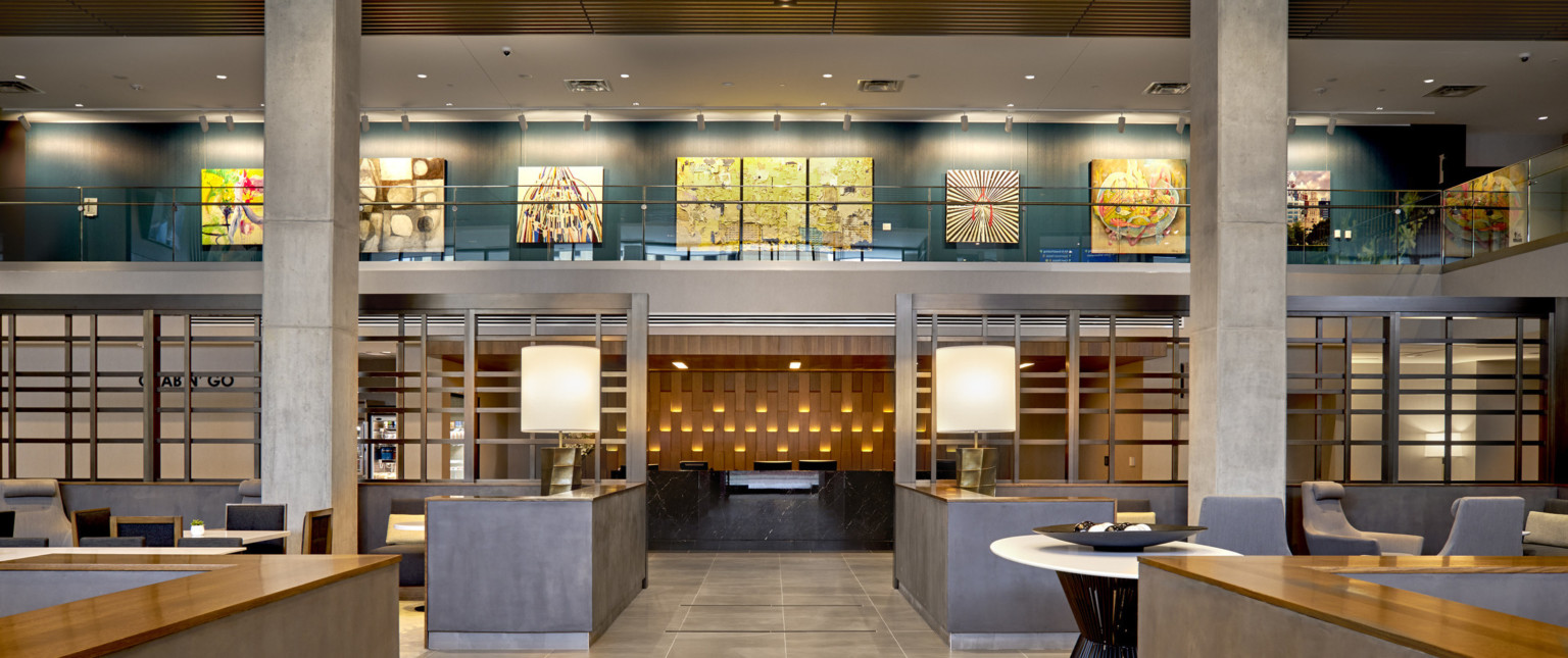 View down mezzanine hallway to reception desk. Wood panel wall mirrors texture of white exterior paneling, with lights at top