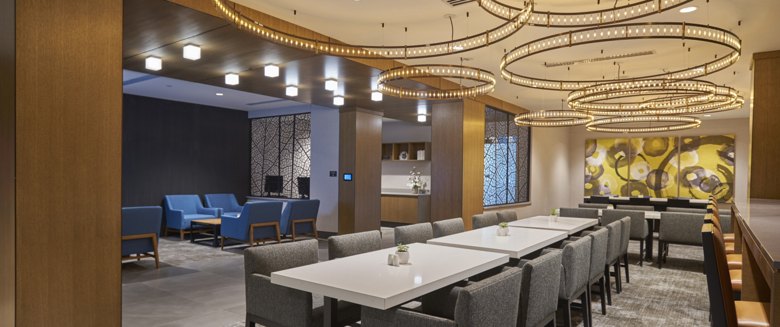 Long white tables with grey arm chairs with layer round chandeliers overhead. Adjoining grey room with blue chairs and table