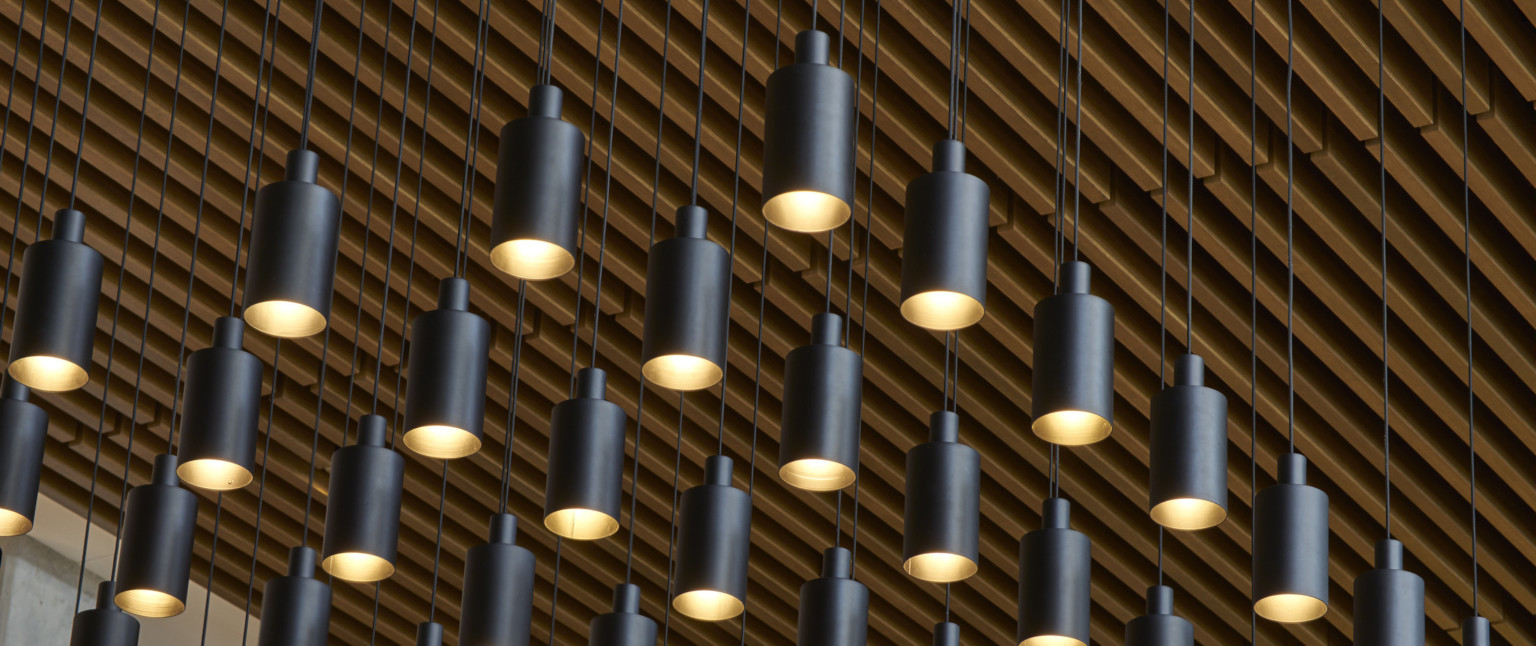 Close up view of rows of black pendant lights hanging from wood slat ceiling