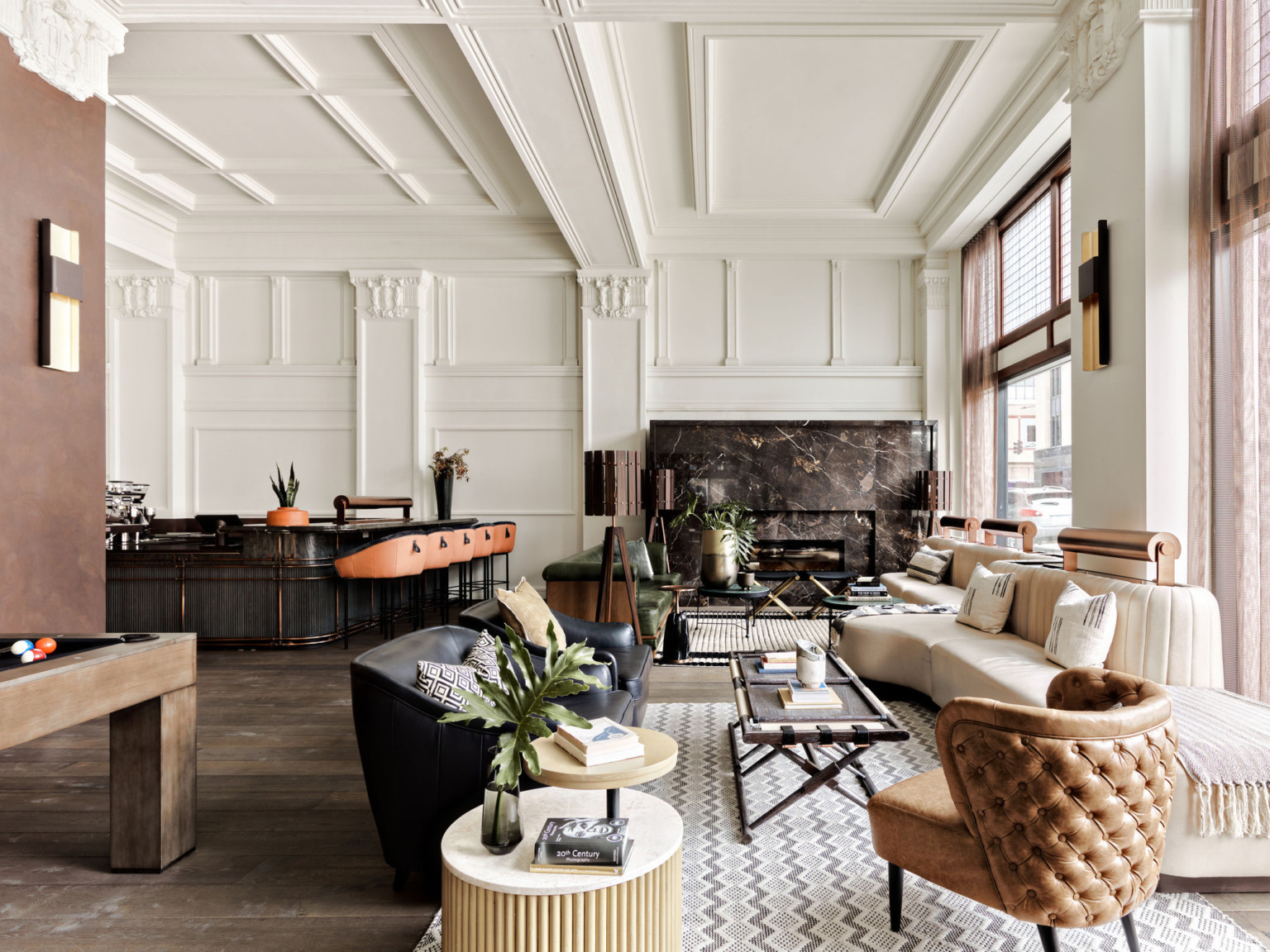 Seating area with arm chairs and cushioned bench along windows. Dark marbled fireplace on white wall with pillars and molding