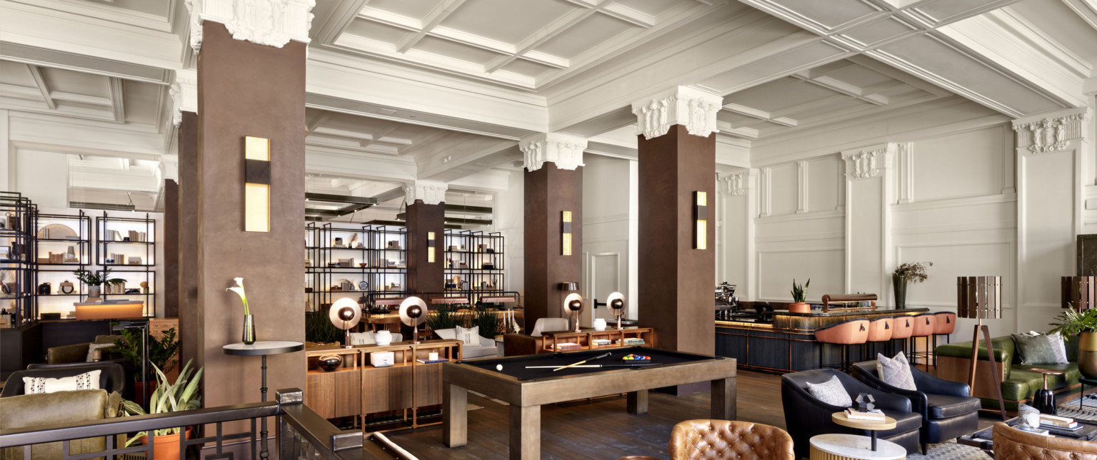 Seating area in the Surety Hotel with wood pillars and white stone capitals in white room with recessed ceiling details.