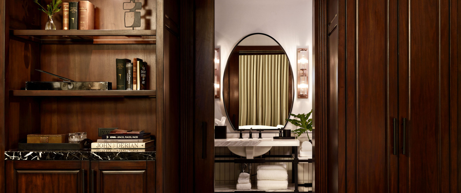 Dark wood shelves and cabinets on either side of pocket door to bathroom with marble sink on black metal base