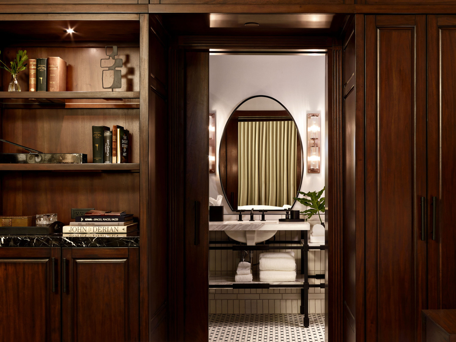 Dark wood shelves and cabinets on either side of pocket door to bathroom with marble sink on black metal base