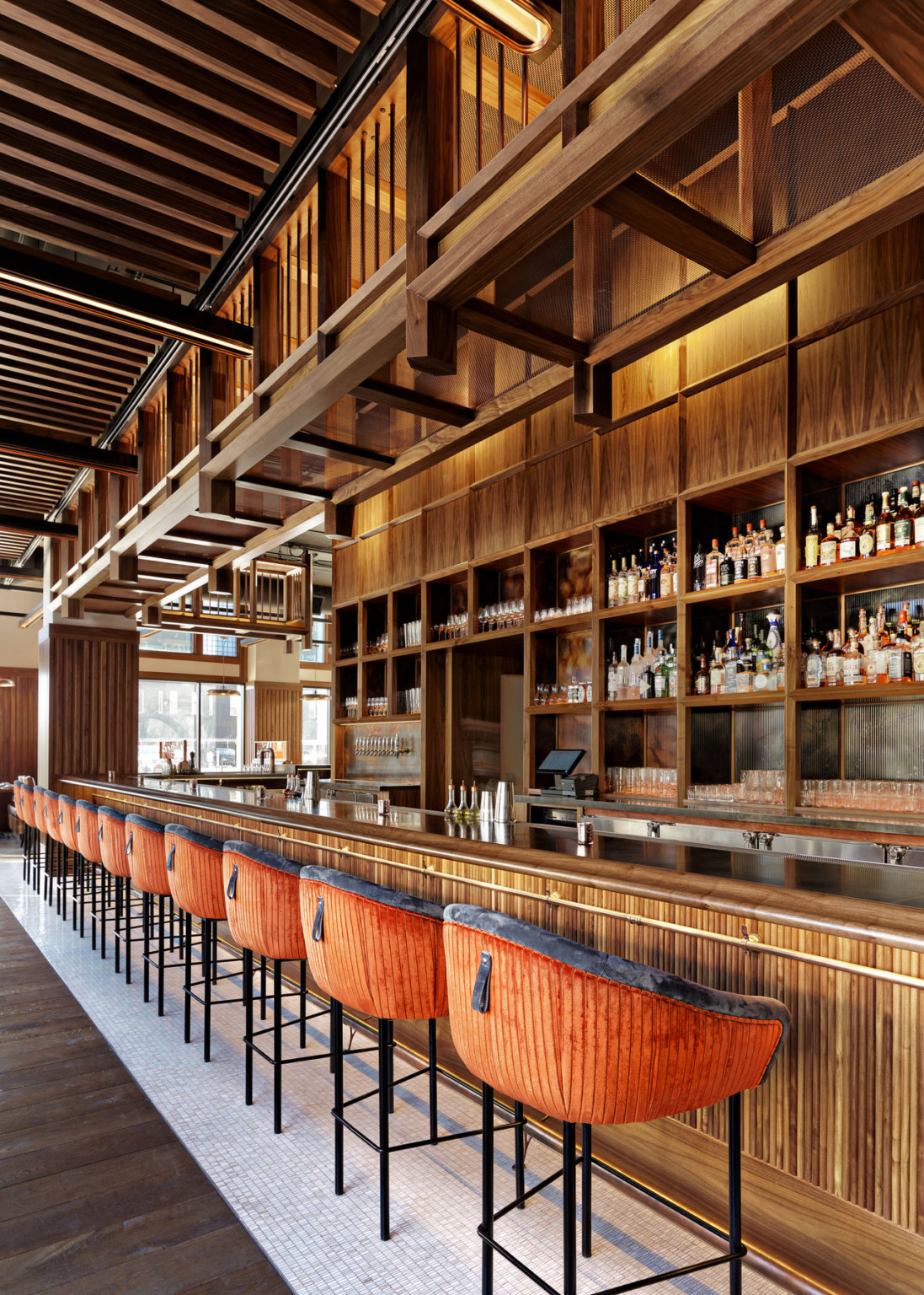 Large wood bar with built in shelves along the back. Wood overhang over back of bar, and stools with red and black upholstery