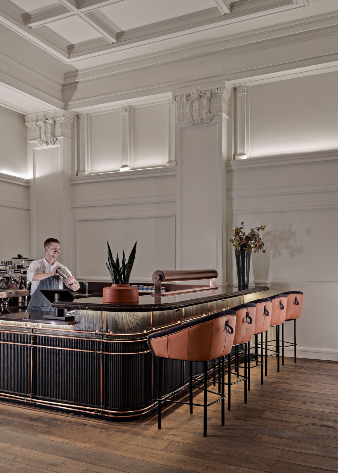 Dark wood bar with stone counter and orange metal details wrapping around. Stools at bar with orange and black upholstery