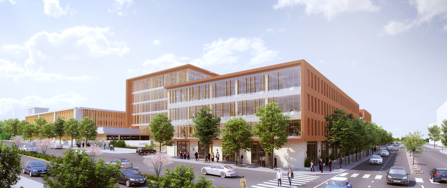 Back corner view of building with white limestone base under glass and wrapped facade. Entrance to parking garage, left