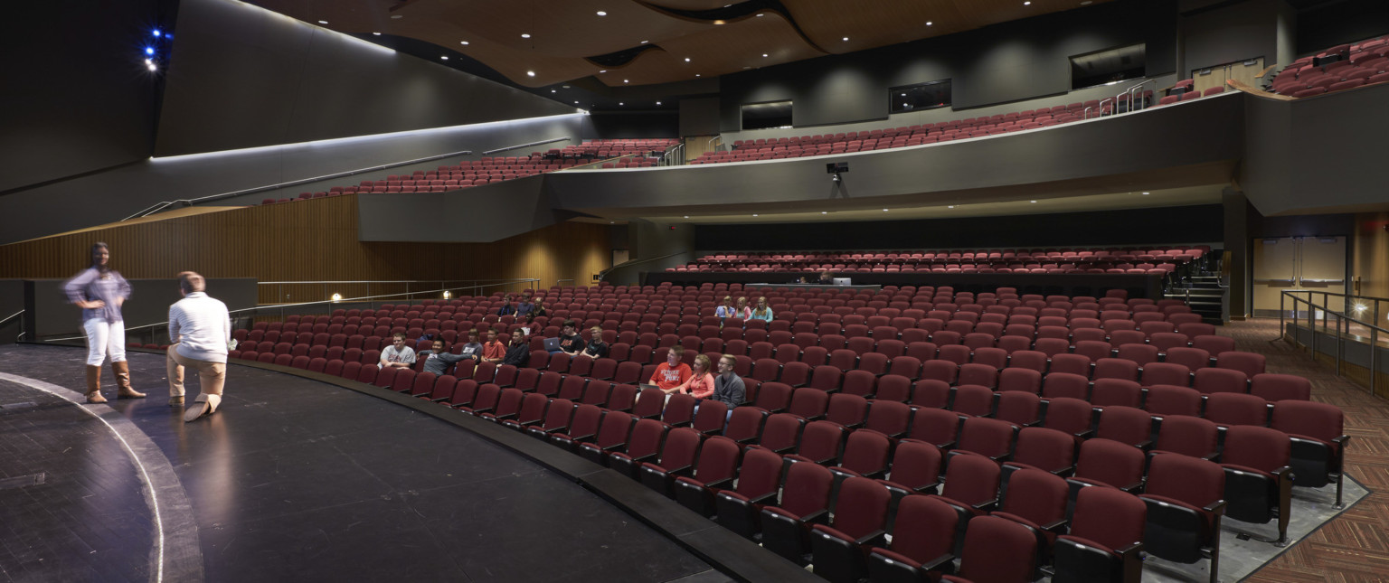 Theater viewed from stage right looking to red theater seats. Black walls with wood accents. Acoustic panels above balcony