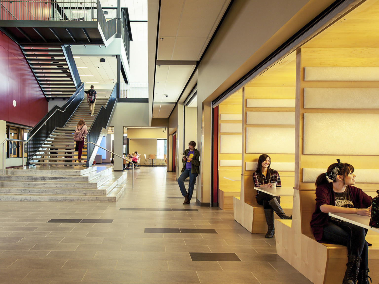 Wood booths recessed into right wall in atrium with stone steps to floating stairs. Flexible wall classroom at end of hall