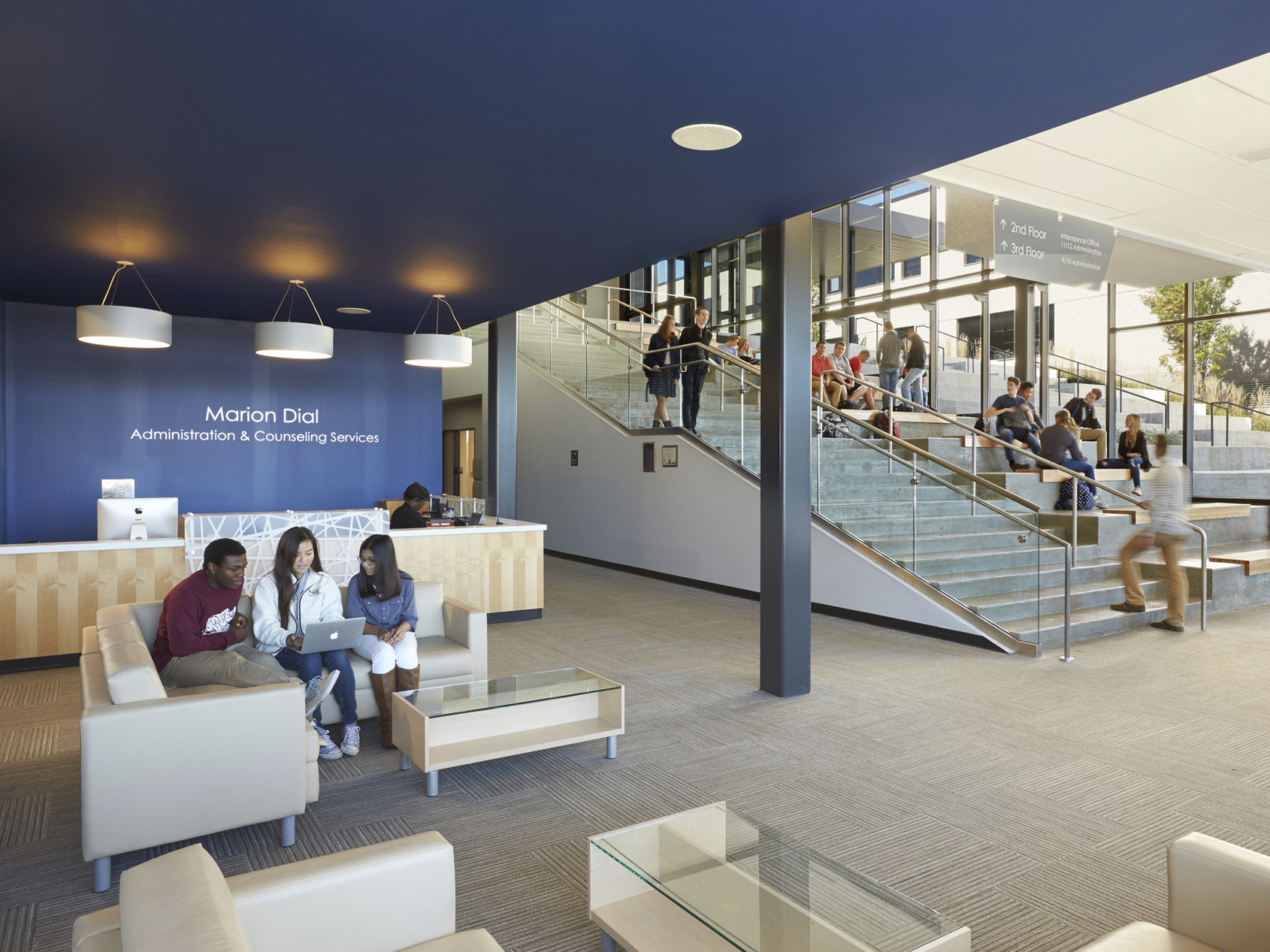 Blue recessed room with wood reception desk and seating to left of main concrete staircase with stepped bench seating